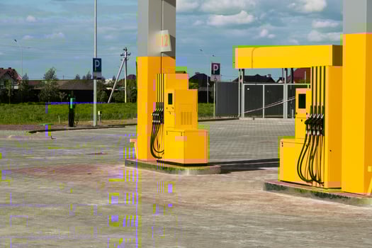 A bright, modern fuel station features yellow pumps set in a spacious, open area under a clear blue sky. Nearby parking spaces are visible, enhancing accessibility photo