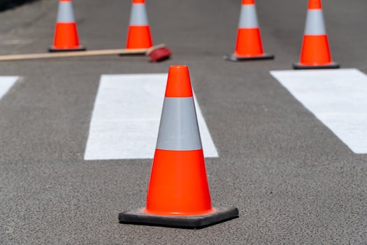 Bright orange traffic cones are placed along a newly painted pedestrian crossing. A construction tool lies nearby, indicating active roadwork in the area photo