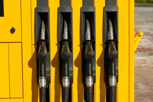 Four pump nozzles are lined up at a gasoline station, showcasing a bright yellow design against a clear daytime backdrop. The area is well-lit and inviting photo