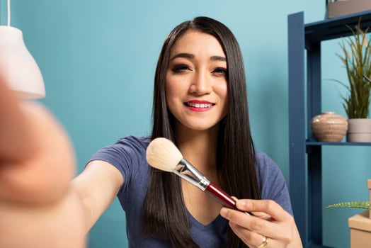 Fashion blogger recording a livestream tutorial, presenting makeup tools and engaging her viewers. She shares insights into cosmetic brushes and makeup techniques for her audience. photo