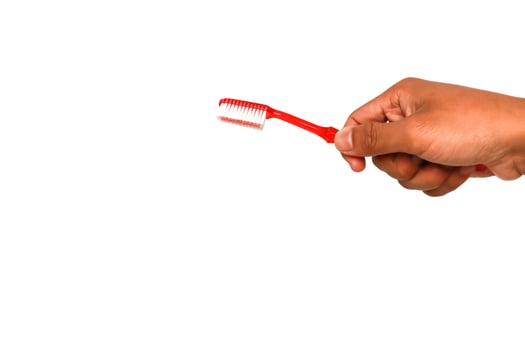 A hand holding a red toothbrush with white bristles against a bright white background ready for oral care photo