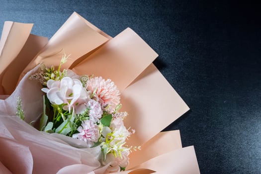Elegant bouquet of pastel flowers wrapped in soft peach paper on black background. Romantic floral arrangement for gift, celebration, wedding, or Valentine's Day. photo