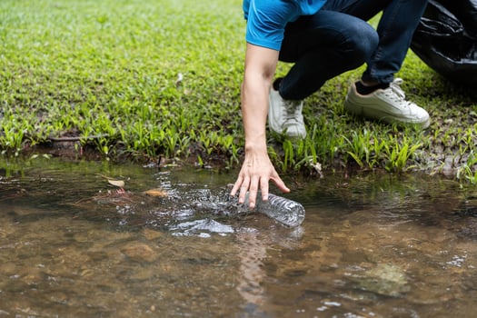 Volunteer Action in Nature. Individual picking up plastic waste from a stream to promote environmental sustainability. photo