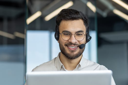 Man with headset close-up smiling, talking and consulting clients remotely. Support service worker at workplace inside office. Consultant at work. photo