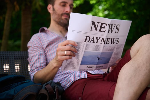 Man Sitting Outdoors Reading a Newspaper in the Park Surrounded by Green Trees photo