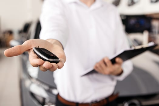 The car dealer hands the car keys towards the camera in a modern dealership. Concept a pivotal moment in the transaction, reflecting the joy and satisfaction of purchasing a car. photo