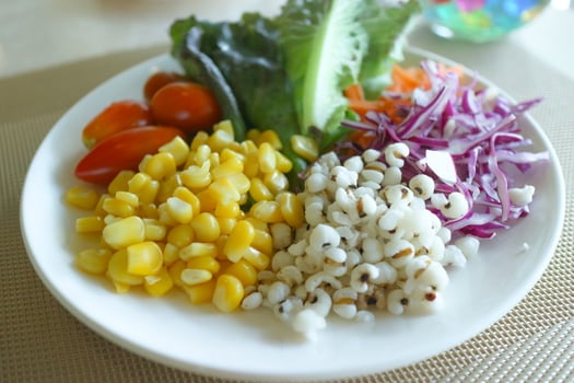 Close-up shot of a healthy vegetable salad with tomatoes, corn, coix seeds, purple cabbage, carrots, and green cos. Beautifully arranged on a golden placemat with a tiny decorative plant. photo