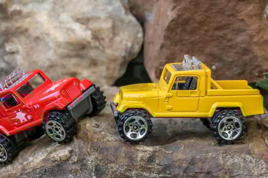 Creative miniature scene of two small 4x4 pickup trucks, yellow and red, appearing to cross paths on rugged rocky mountains. Playful tiny adventure concept with an outdoor exploration vibe. photo