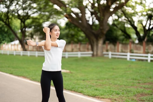 Dynamic Stretching. Young woman stretching arms outdoors in park. photo