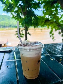 A cup of iced coffee sitting on a table in front of a river photo