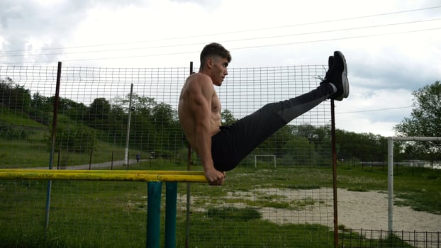 Strong man trains abdominal muscles raising legs on parallel bars at sports groun.Young shirtless sportsman exercising at nature. Sporty athlete working out at nature. Concept of sportive lifestyle photo