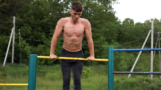 Hardy shirtless sportsman doing push ups on horizontal bar at nature. Strong and muscular guy training at sports ground. Young athletic guy exercising outdoor. Concept of active and healthy lifesty photo