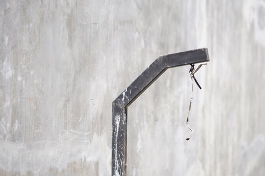 A dirty black pole with exposed wires near a gray wall during the day photo