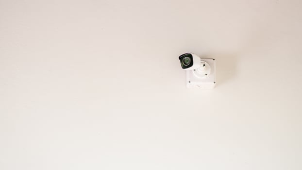 A sleek security camera mounted on a white ceiling, showcasing modern surveillance technology in a minimalist setting. photo