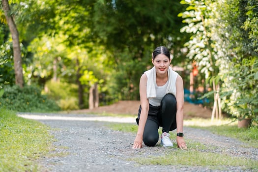 Woman in athletic wear kneeling on a gravel path, ready to run, with vibrant green trees and grass in the background. photo