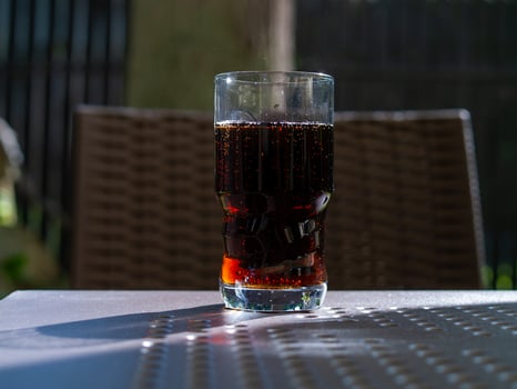 Glass of soda sits on a table in the sun photo