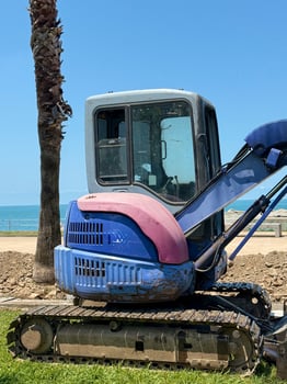 Vibrant Excavator Framed by Palm Trees on Coastal Grassland photo