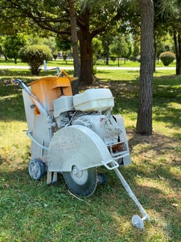 Concrete Saw Positioned on Grass Amid Parkside Foliage photo