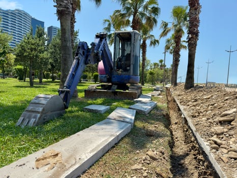 Small Excavator and Concrete Slabs Beside Trench on Grassy Lot photo