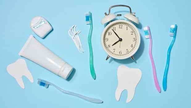 White tube of toothpaste, dental floss in a case, toothbrushes of different colors, white alarm clock, plastic flossers placed on a blue background. Top view. photo
