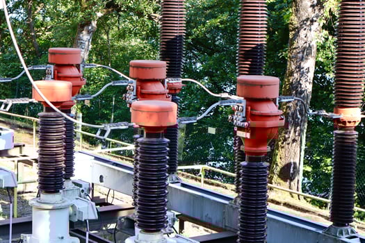 Close-up of a power transformer with cooling fins, high-voltage insulators, and overhead wires. Industrial electricity infrastructure under blue sky. photo
