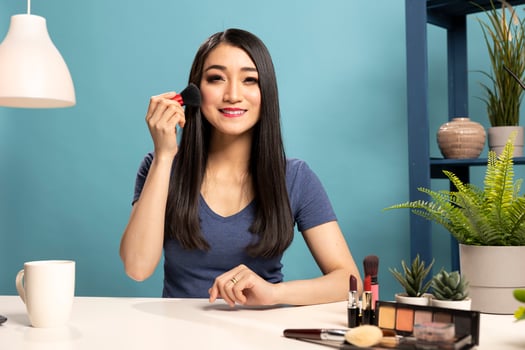 Friendly beauty influencer conducting an online makeup tutorial and demonstrating different ways to use a brush. Asian content creator in her studio, livestreaming about cosmetic tools. photo