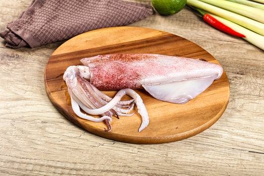 A squid on a wooden cutting board with a knife and a bunch of other vegetables photo