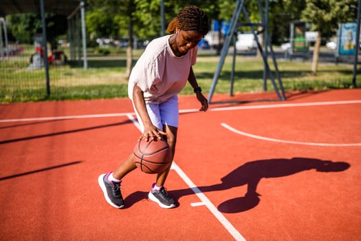 A focused female athlete practices dribbling and ball control on a basketball court under the bright summer sun, enjoying the sport and urban environment. photo
