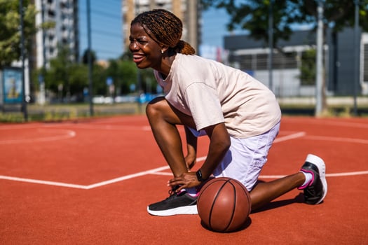 Young African American woman grimacing in pain after twisting her ankle on urban basketball court during practice. photo