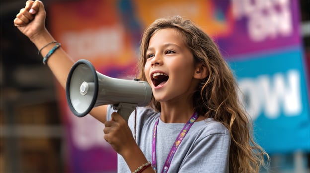 A young girl with long hair raises one arm in excitement while holding a megaphone, actively cheering at a lively outdoor event surrounded by colorful banners. photo