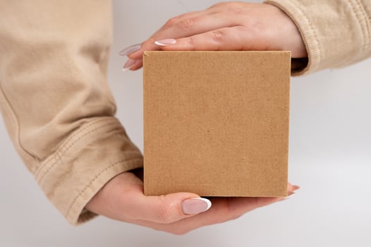 Woman holding plain brown box with hands displaying neutral manicure. National Cartonnage Day photo