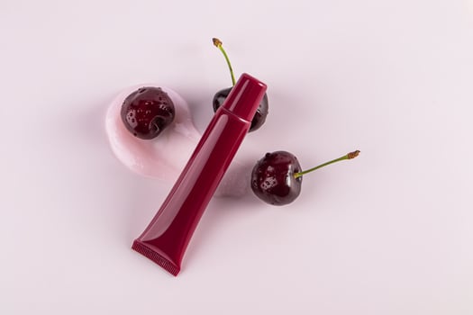 Cosmetic packaging A tube of cherry lip balm lies on a balm sample among ripe cherries. top view. Blank packaging layout. pink background photo