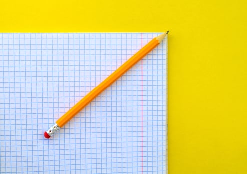 White notebook in a cage and a pencil on a yellow background. photo