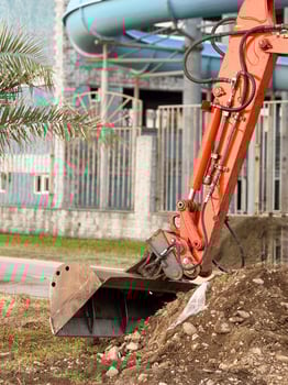 Excavator Digging beside Blue Water Slide and Urban Structures photo