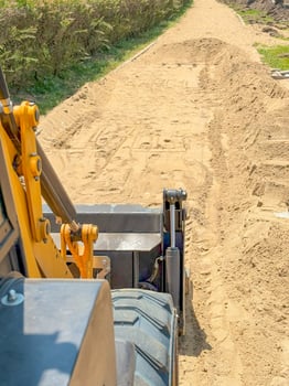 Bulldozer Pushing Sand on Narrow Urban Worksite with Green Backdrop photo
