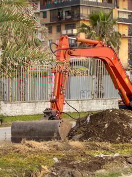 Urban Excavator Scooping Dirt Beside Palm Tree and Fence photo