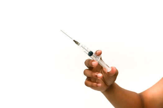 A dark-skinned hand holds a syringe on a white background representing medical treatment and vaccination photo