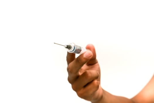 Close-up of a hand holding a syringe against a clean, white background for medical use photo
