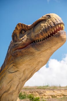 Huge Artificial dinosaur tyrannosaurus, close-up of dinosaur head against sky. With copy space. Dinosaur shows its teeth, yellow rocks and trees in the background photo