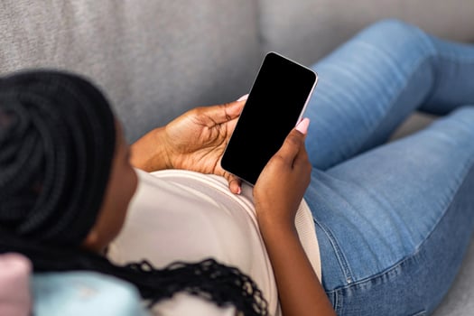 Unrecognizable african american woman laying on sofa at home and using modern smartphone with blank screen, mockup, copy space. Black lady looking at mobile phone empty display photo