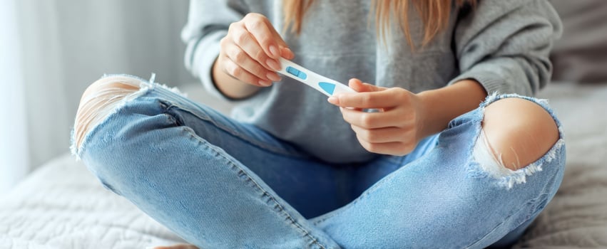 The woman holding a pregnancy test while sitting on a bed. photo