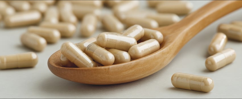 The wooden spoon holding beige capsules against a soft background. photo
