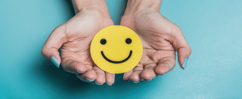 The cheerful smiley face held in hands against a vibrant blue background. photo