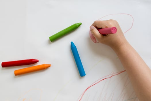Child coloring with bright crayons on white paper photo