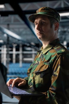 Military officer managing logistics operations using laptop in server room command center. Soldier wearing uniform running diagnostics on infrastructure in army data center photo