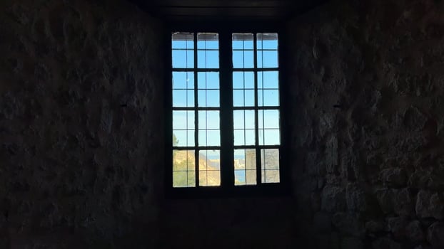 A beautifully crafted window frame offers a picturesque view of nature beyond a historic stone wall photo
