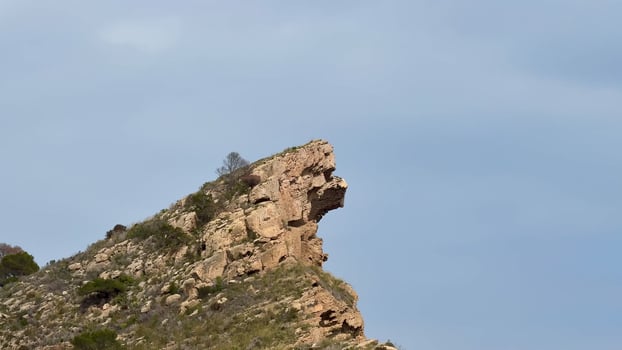 A striking rock formation resembling a human profile in a majestic mountainous landscape under a clear sky photo