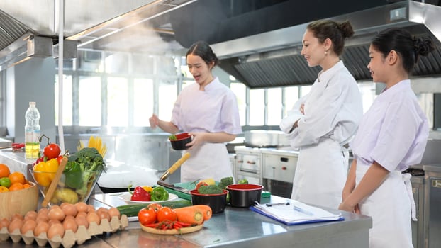 Young Chefs Learning and Cooking in a Professional Kitchen, Culinary Students Practicing Cooking Skills with Instructor, Three Female Cooks Preparing Food in a Commercial Kitchen photo