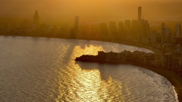 Aerial view of a vibrant city skyline illuminated by warm golden hour light over a calm, tranquil sea photo