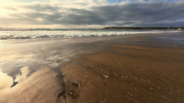 A tranquil beach view displays gentle waves lapping on warm sand beneath a dramatically cloudy sky above photo